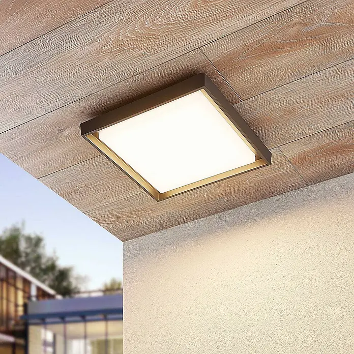 Lucande LED Outdoor Deckenlampe in dunkelgrau, weiß, Deckenleuchte außen -  - Quadratische Deckenleuchte mit dunklem Rahmen und goldenem Akzent an Holzdecke, beleuchtet eine Texturwand im Außenbereich.