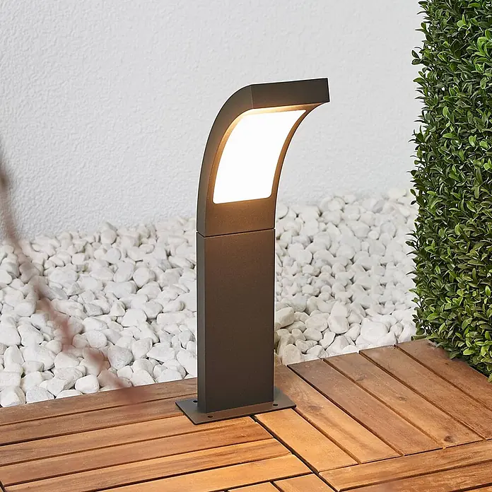 Lucande Außensockelleuchte Juvia -  - Moderne dunkelgraue Außenstehleuchte mit beleuchteter geschwungener Oberseite, auf Holzterrasse platziert.