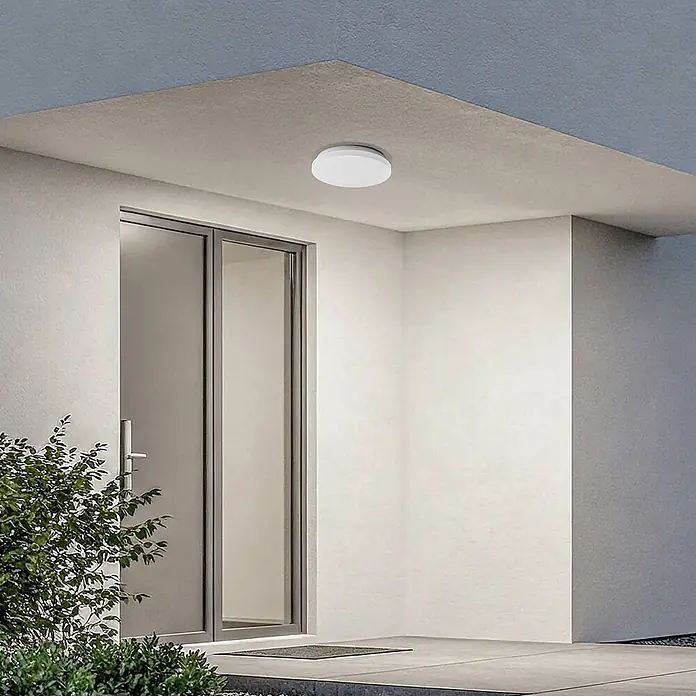 Lindby LED Outdoor Deckenlampe in weiß, mit Bewegungsmelder, Deckenleuchte -  - Weiße, runde LED-Deckenleuchte, an einer Außenüberdachung montiert, beleuchtet den Eingangsbereich über einer Glastür.