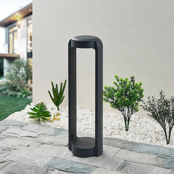 Lucande Außensockelleuchte Habsa -  - Dunkelgraue Outdoor-Pollerleuchte auf einer Terrasse mit Zierkies und Pflanzen.