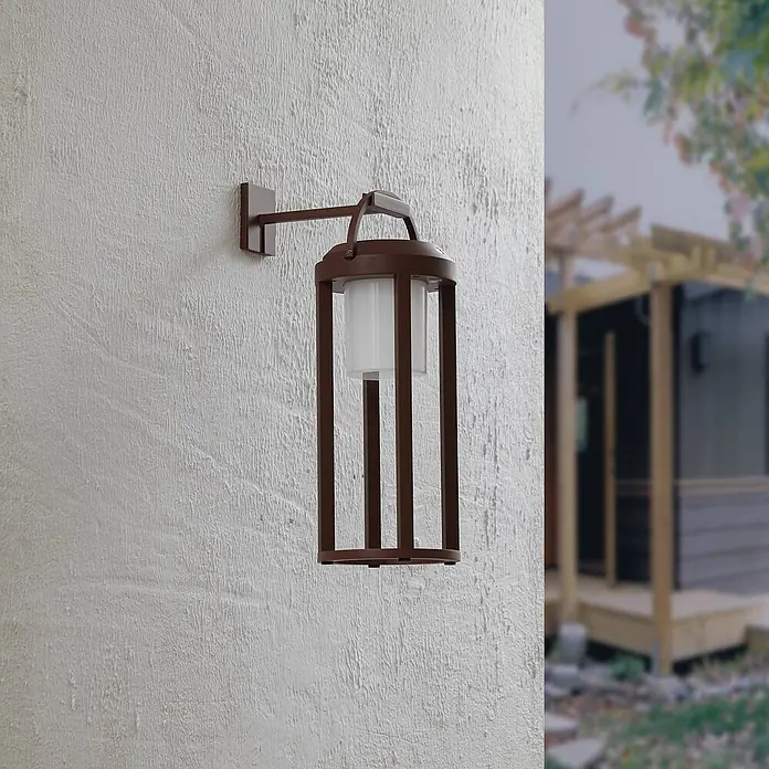 Lucande LED Solar Wandleuchte aussen in rost, weiß, dimmbar Aussenlampe -  - Braune Außenwandlaterne mit weißem Diffusor, an einer strukturierten Wand, in einer Außenumgebung.