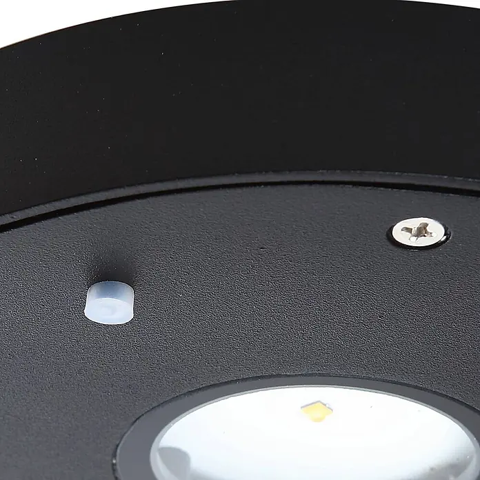 Lucande Außenwandleuchte Tavon - schwarz, schwarz, IP54 - Schwarzes strukturiertes Gerät mit lichtdurchlässigem Knopf, silberner Schraube und weißem LED-Licht.