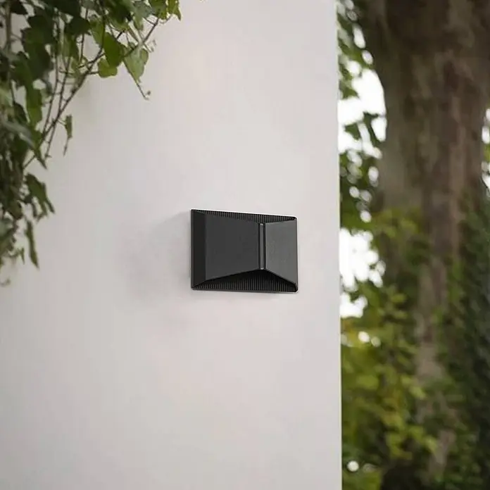Lindby LED Wandleuchte aussen in schwarz, Aussenlampe Wand -  - Schwarze geometrische Außenwandleuchte, an einer Wand montiert, umgeben von Laub.
