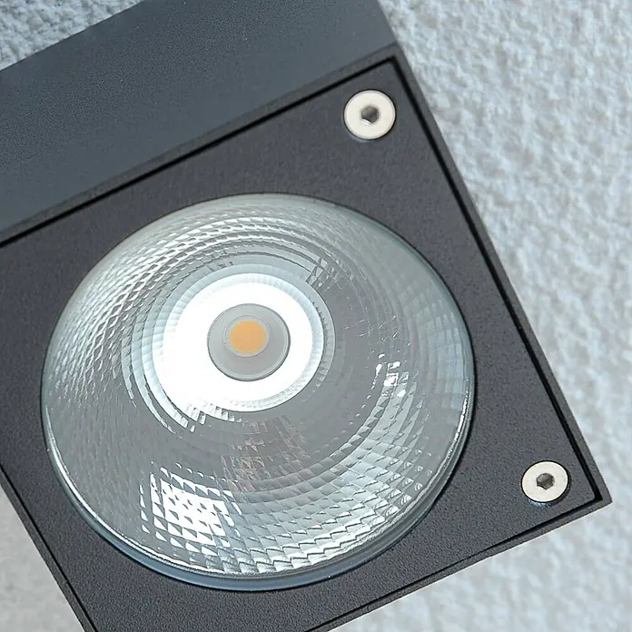 Lucande LED Outdoor Deckenlampe in graphit, Deckenleuchte außen -  - Nahaufnahme eines schwarzen, quadratischen LED-Strahlers mit texturierter Glaslinse, warmweißem LED-Chip und zwei Silberschrauben an einer hellen Wand.