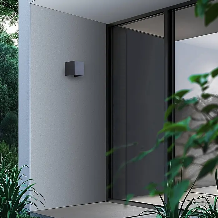 Lindby LED Wandleuchte aussen Smart Home in dunkelgrau, dimmbar up down -  - Dunkelgraue, kubische Außenwandleuchte an einer modernen Fassade neben einer Glastür.