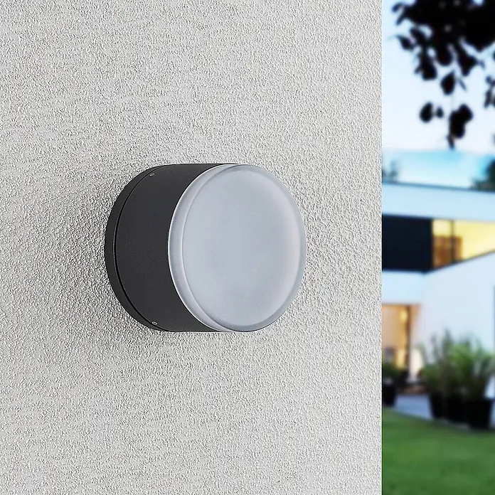Lindby LED Wandleuchte aussen in dunkelgrau, weiß, Aussenlampe Wand -  - Runde dunkelgraue Außenwandleuchte mit mattierter weißer Abdeckung, an einer weißen Strukturwand neben einem modernen Haus montiert.