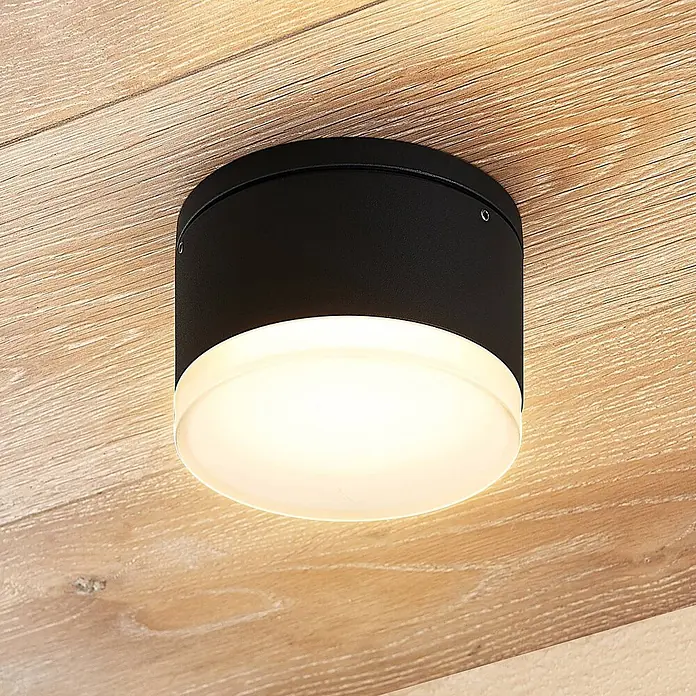 Lindby LED Wandleuchte aussen in dunkelgrau, weiß, Aussenlampe Wand -  - Schwarze zylindrische Deckenleuchte mit weißem Diffusor, an einer Holzoberfläche montiert.