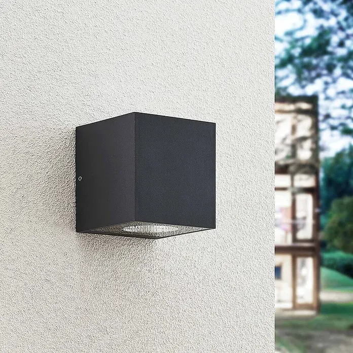 Arcchio LED Wandleuchte aussen in anthrazit, Aussenlampe Wand -  - Anthrazitfarbene, würfelförmige Außenwandleuchte, die an einer strukturierten Wand montiert ist und nach unten leuchtet.