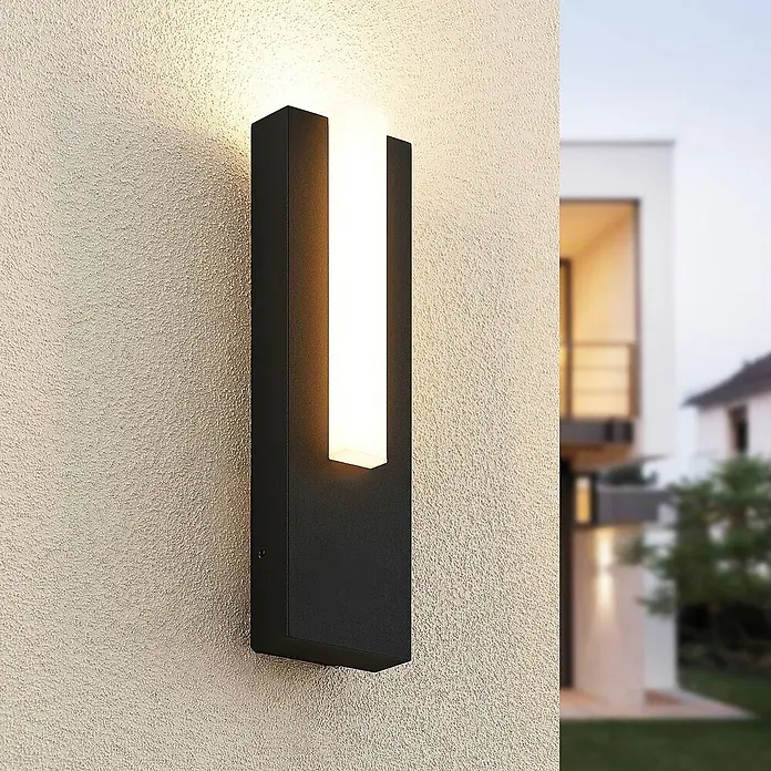 Lucande LED Wandleuchte aussen in anthrazit, weiß, Aussenlampe Wand -  - Moderne schwarze Außenwandleuchte mit vertikalem weißen Lichtstreifen, an einer texturierten Hauswand montiert und warm leuchtend.