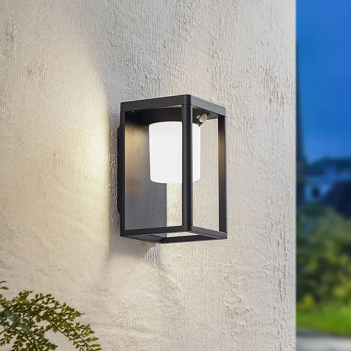 Lucande Außenwandleuchte Tilena - schwarz, IP54 - Schwarze Außenwandleuchte aus Metall mit weißem Diffusor und Bewegungsmelder an einer strukturierten Wand.