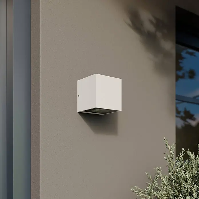 Arcchio LED Wandleuchte aussen in weiß, Aussenlampe Wand -  - Weißer kubischer Außenwandstrahler an beiger Fassade, Licht nach unten werfend, mit grünen Pflanzen.