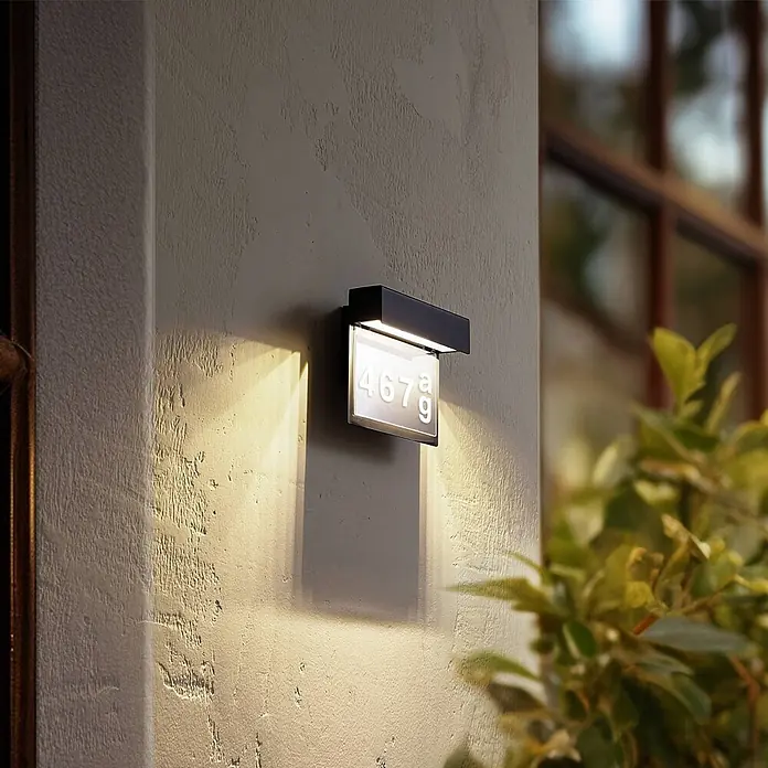 Lindby LED Wandleuchte aussen in dunkelgrau, Aussenlampe Wand -  - Schwarze Außenwandleuchte beleuchtet Hausnummer 467g an einer strukturierten Wand.