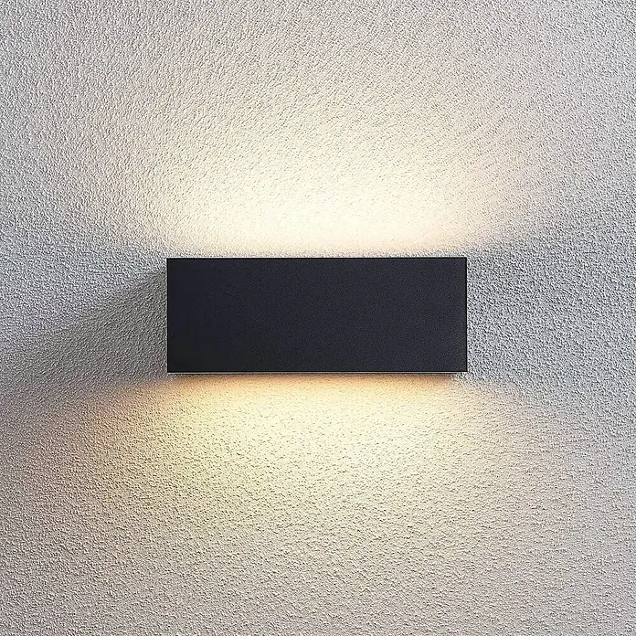 Lindby LED Wandleuchte aussen in dunkelgrau, weiß, Aussenlampe Wand -  - Eine schwarze, rechteckige Außenwandleuchte an einer strukturierten Wand, die warmes Licht nach oben und unten wirft.