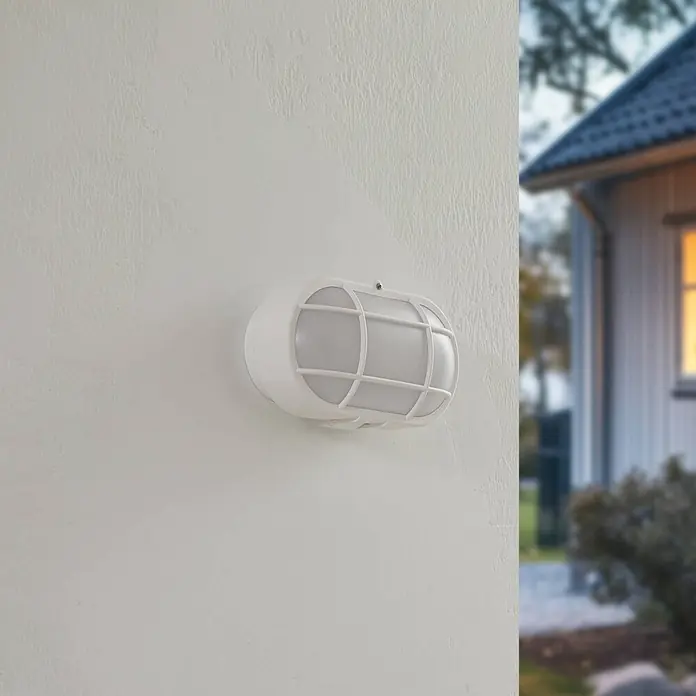 Lindby LED Wandleuchte aussen in weiß, Aussenlampe Wand -  - Weiße ovale Außenwandleuchte mit Gitterabdeckung an einer strukturierten Wand.