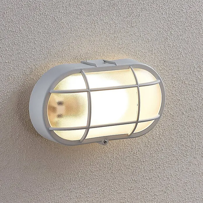 Lindby LED Wandleuchte aussen in weiß, Aussenlampe Wand -  - Beleuchtete graue ovale Außenwandleuchte mit Schutzgitter und mattierter Abdeckung, an einer strukturierten Wand montiert.