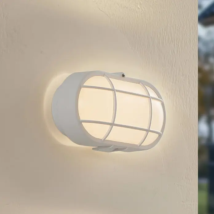 Lindby LED Wandleuchte aussen in weiß, Aussenlampe Wand -  - Weiße ovale Außenwandleuchte mit Gitter, beleuchtet eine strukturierte Wand.