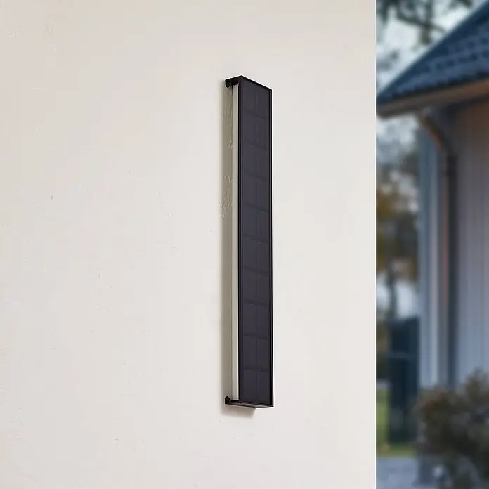 Lindby LED Solar Wandleuchte aussen in schwarz, weiß, dimmbar Aussenlampe -  - Ein schwarzes, rechteckiges solarbetriebenes Außenlicht ist vertikal an einer hellen Wand montiert und hat eine strukturierte Solarpanel-Oberfläche.