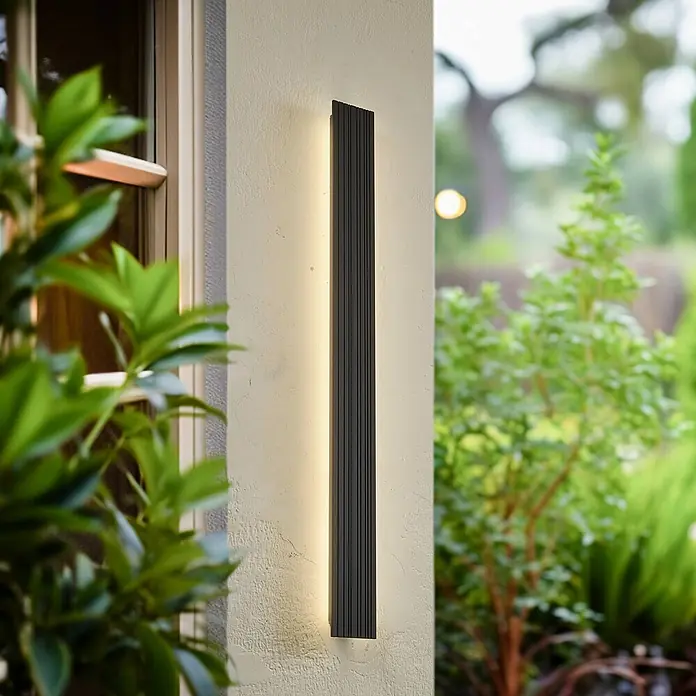 Lucande LED Wandleuchte aussen in schwarz, Aussenlampe Wand -  - Schwarze, vertikale Außenwandleuchte mit Rippenstruktur, warmes Licht auf einer Fassade.