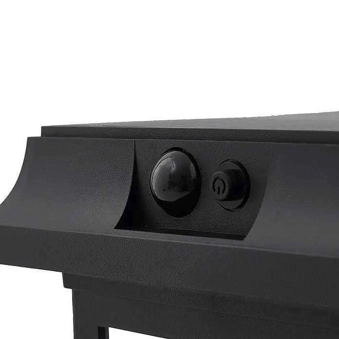 Lindby LED Solar Wandleuchte aussen in schwarz, mit Bewegungsmelder, -  - Nahaufnahme einer schwarzen, texturierten Leuchte mit glänzendem Sensor und Ein-/Ausschalter.