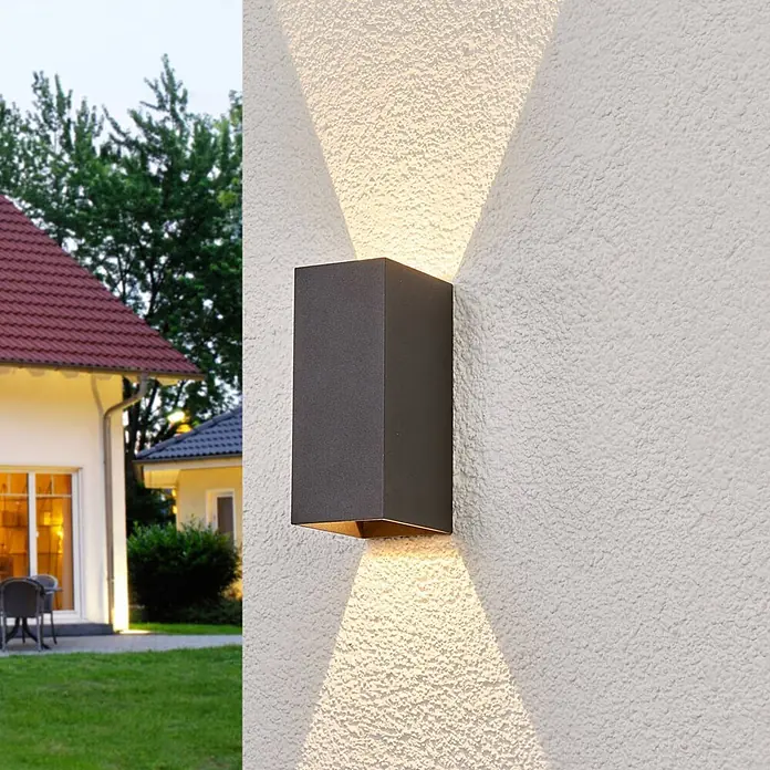 Lucande LED Wandleuchte aussen in anthrazit, Aussenlampe Wand -  - Dunkelgraue, rechteckige Außenwandleuchte, die warme Lichtstrahlen nach oben und unten auf eine strukturierte Fassade im Garten wirft.