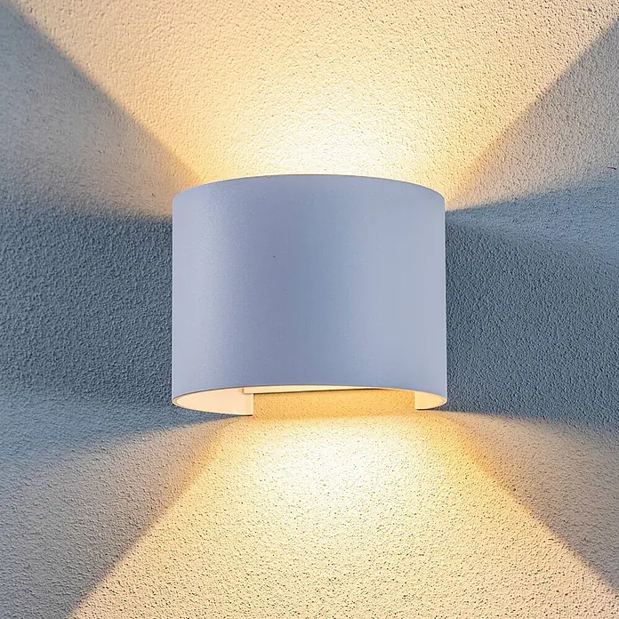 Lindby LED Wandleuchte aussen in weiß, up down Aussenlampe Wand -  - Weißes zylindrisches Wandlicht an einer strukturierten Wand, das warmes Licht nach oben und unten abstrahlt.