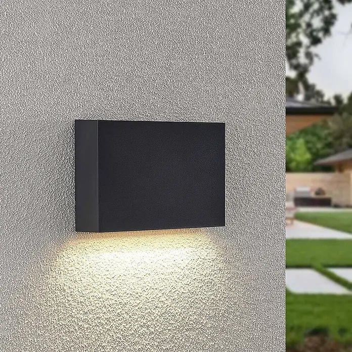 Lindby LED Wandleuchte aussen in dunkelgrau, Aussenlampe Wand -  - Schwarze, rechteckige Außenwandleuchte, die warmes Licht nach unten auf eine strukturierte Wand wirft.