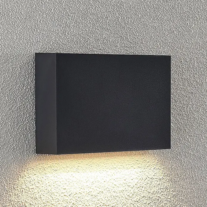 Lindby LED Wandleuchte aussen in dunkelgrau, Aussenlampe Wand -  - Rechteckige, dunkelgraue Außenwandleuchte, die warmes Licht nach unten auf eine strukturierte Wand wirft.