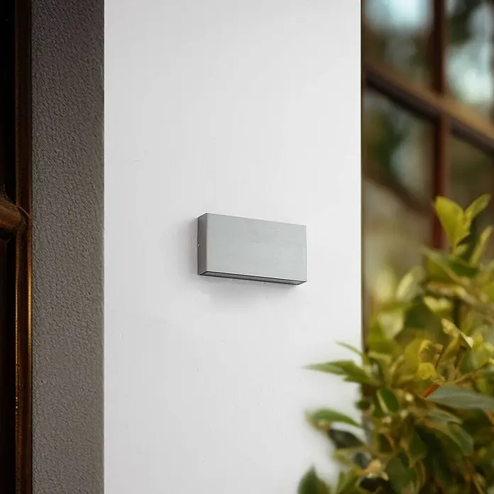 Lindby Außenwandleuchte Jarte - chrom / silber, IP54 - Rechteckige silber-graue gebürstete Metall-Außenleuchte an einer Wand montiert.