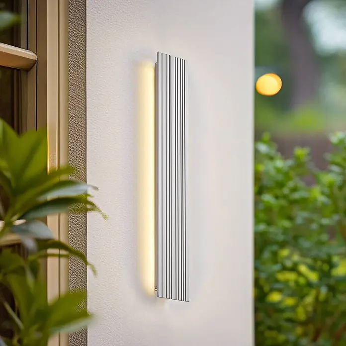 Lucande Außenwandleuchte Melira - alu / grau / zink, alu / grau / zink, IP65 - Silbernfarbene Außenwandleuchte mit vertikalen Rillen, warmes Licht abgebend, an einer Außenwand montiert.