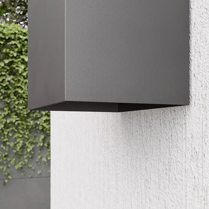 Lucande LED Wandleuchte aussen in dunkelgrau, Aussenlampe Wand -  - Dunkelgraue, rechteckige Außenwandleuchte mit strukturierter Oberfläche, an weißer Wand neben grünem Laub.