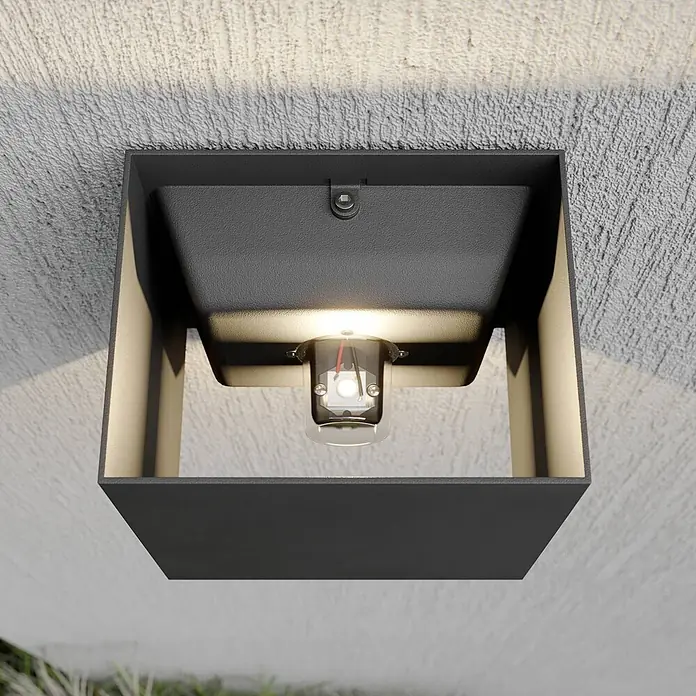 Lucande LED Wandleuchte aussen in dunkelgrau, Aussenlampe Wand -  - Quadratische dunkelgraue Außenwandleuchte mit reflektierendem Inneren, die warmes Licht auf eine strukturierte Wand strahlt.