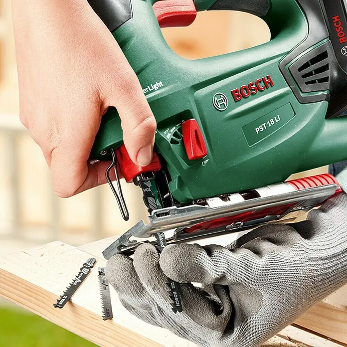 Bosch Power for All 18V Sierra de calar de batería PST 18 LI - 18 V, Iones de litio, 2,5 Ah, 1 batería, 0 /min - 2.400 /min - Primer plano de una sierra de calar Bosch PST 18 LI sostenida por manos enguantadas, en uso sobre una tabla de madera.