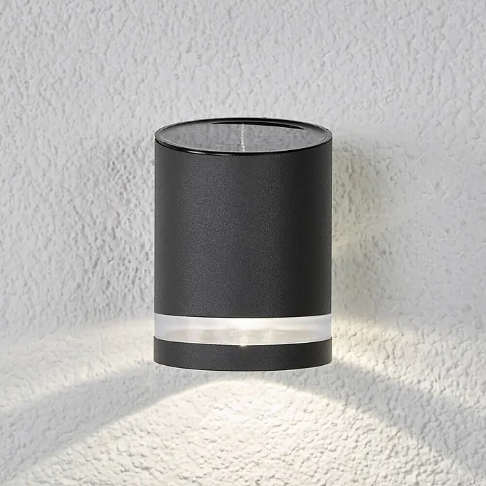 Lindby Solar LED Wandlampe / Wandleuchte außen, 1x 0,5W LED, Downlight -  - Schwarze zylindrische Solar-Wandleuchte mit transluzentem Band, an einer texturierten Wand montiert und nach unten strahlend.
