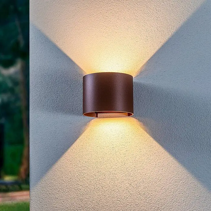 Lindby LED Wandleuchte aussen in rost, up down Aussenlampe Wand -  - Dunkelbronzene zylindrische Außenwandleuchte beleuchtet eine strukturierte Wand mit Auf- und Abwärtsstrahlen.