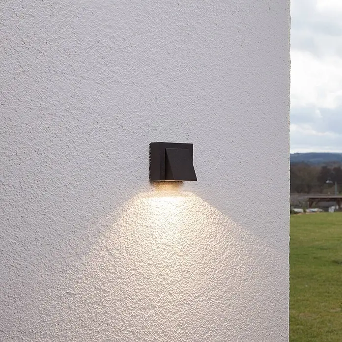 Lucande Außenwandleuchte Marik - schwarz, schwarz, IP54 - Dunkle quadratische Außenwandleuchte an texturierter Wand, die warmes Licht nach unten wirft.