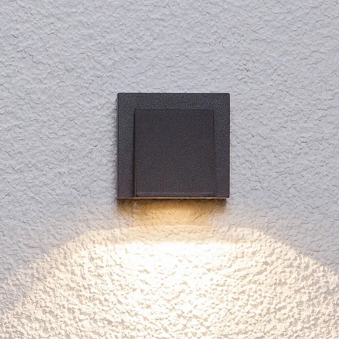 Lucande Außenwandleuchte Marik - schwarz, schwarz, IP54 - Dunkelgraue, quadratische Außenwandleuchte an einer strukturierten Wand mit warmer Abwärtsbeleuchtung.