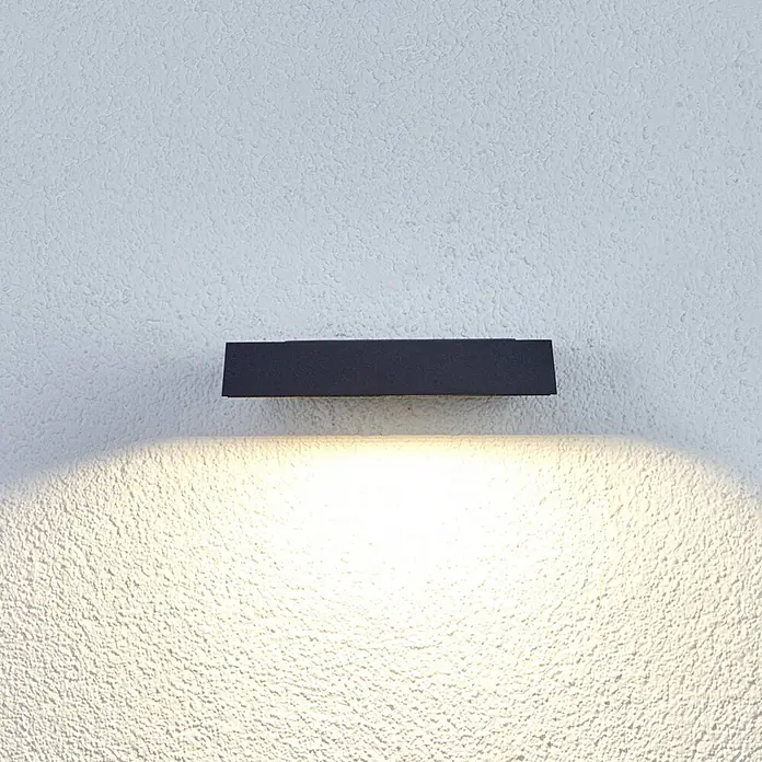 Lucande LED Wandleuchte innen in anthrazit, Wandstrahler -  - Dunkelgraue rechteckige Wandleuchte an einer strukturierten Wand, die ein warmes Licht nach unten wirft.