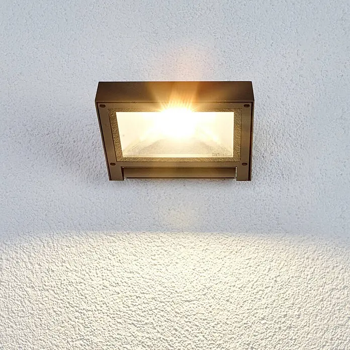 Lucande LED Wandleuchte innen in anthrazit, Wandstrahler -  - Rechteckige dunkelbronzene Außenwandleuchte an texturierter Wand, die warmes Licht nach unten wirft.