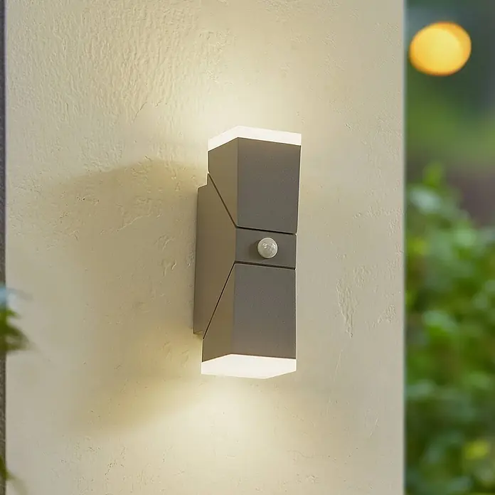 Lindby Außenwandleuchte Sally - alu / grau / zink, alu / grau / zink, IP54 - Dunkelgraue Außenwandleuchte mit Up/Down-Beleuchtung und Bewegungsmelder, an einer strukturierten Wand montiert.