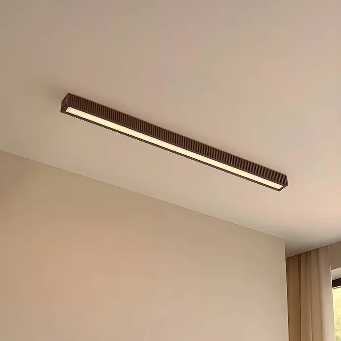 Lucande LED Deckenlampe in dunkelbraun, schwarz, Deckenleuchte -  - Lange, dunkelbraune lineare Deckenleuchte mit geriffelter Textur und warmweißer Beleuchtung in einem modernen Raum montiert.