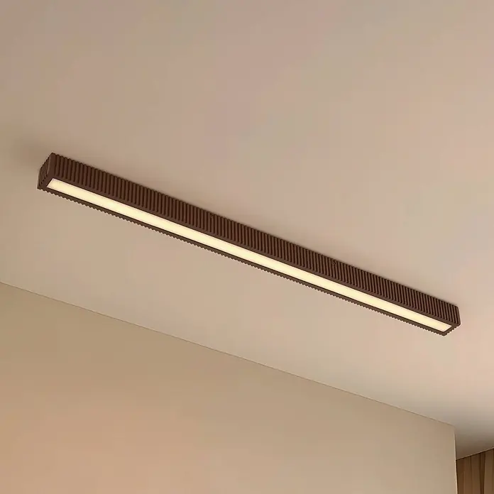 Lucande LED Deckenlampe in dunkelbraun, schwarz, Deckenleuchte -  - Braune, gerippte lineare LED-Deckenleuchte an heller Decke, strahlt warmes Licht aus.