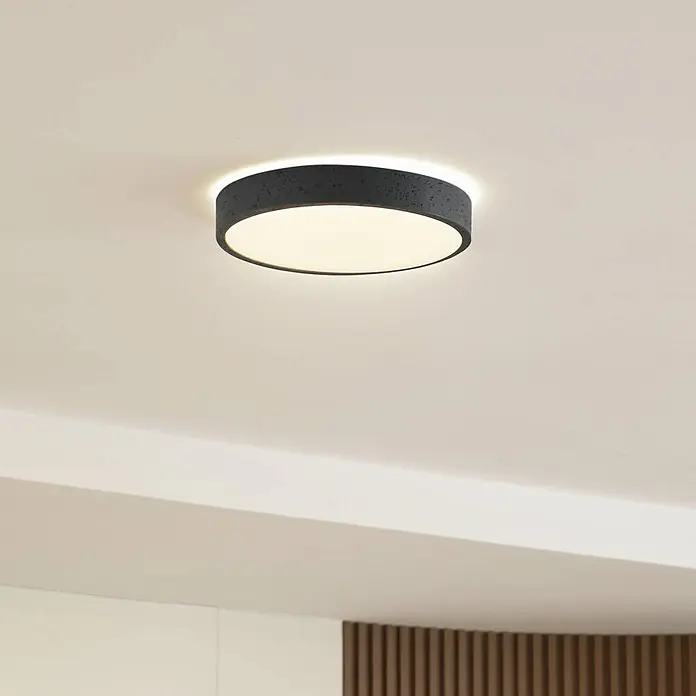 Lindby Deckenleuchte Manala - alu / grau / zink - Eine runde, dunkelgraue, texturierte Deckenleuchte mit weißem Diffusor, an einer hellen Decke montiert und beleuchtet.
