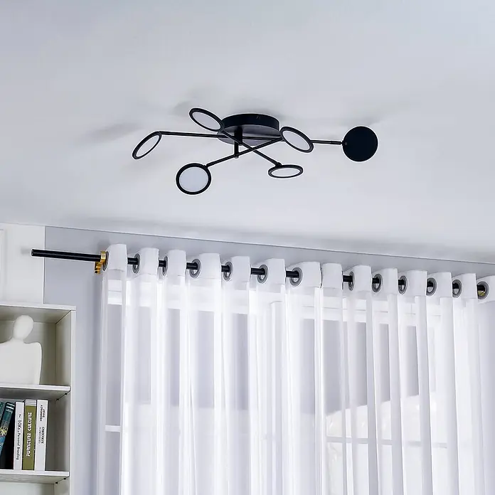 Lindby Deckenleuchte Manel - schwarz, schwarz - Moderne schwarze Deckenleuchte mit mehreren runden Lampen, über transparenten weißen Vorhängen und einem weißen Regal.
