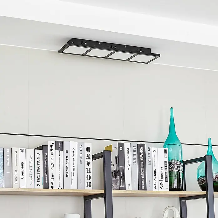 Lindby Deckenleuchte Raymie - schwarz - Schwarze rechteckige LED-Deckenleuchte mit vier quadratischen Panels, die einen Raum über einem Bücherregal beleuchtet.