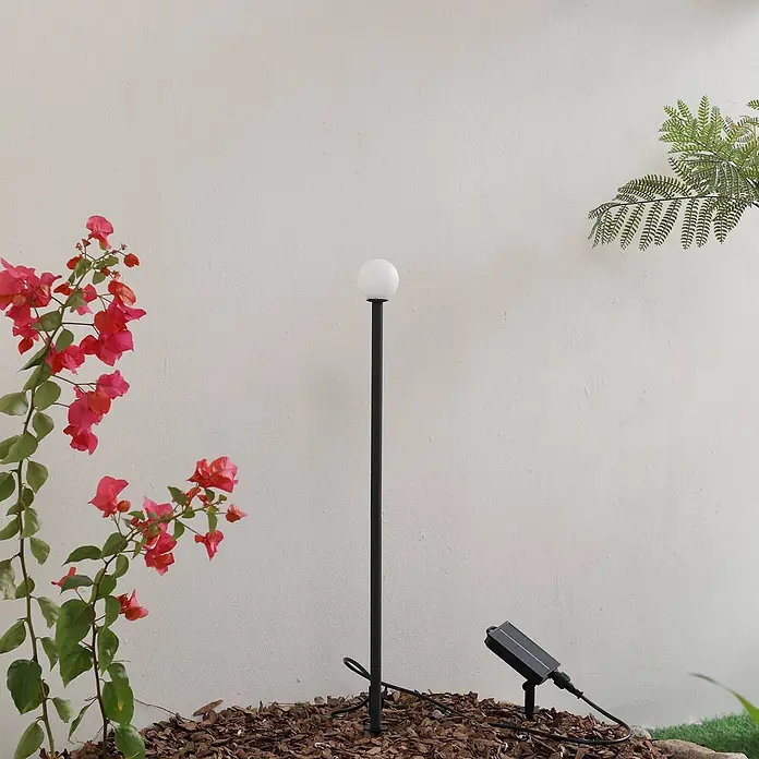Lindby LED Solar Gartenlampe Erdspieß in schwarz matt, Erdspießlampe -  - Schwarze Solar-Gartenleuchte mit kugelförmigem weißem Leuchtenkopf und separatem Solarpanel, in Gartenmulch.