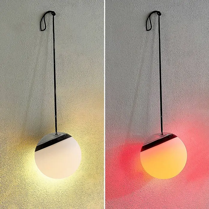 Lindby LED Hängelampe außen in weiß, schwarz, dimmbar Pendelleuchte -  - Eine kugelförmige Hängelampe mit Chromoberteil und schwarzem Kabel beleuchtet eine strukturierte Wand mit warmweißem und rot-orangem Licht.