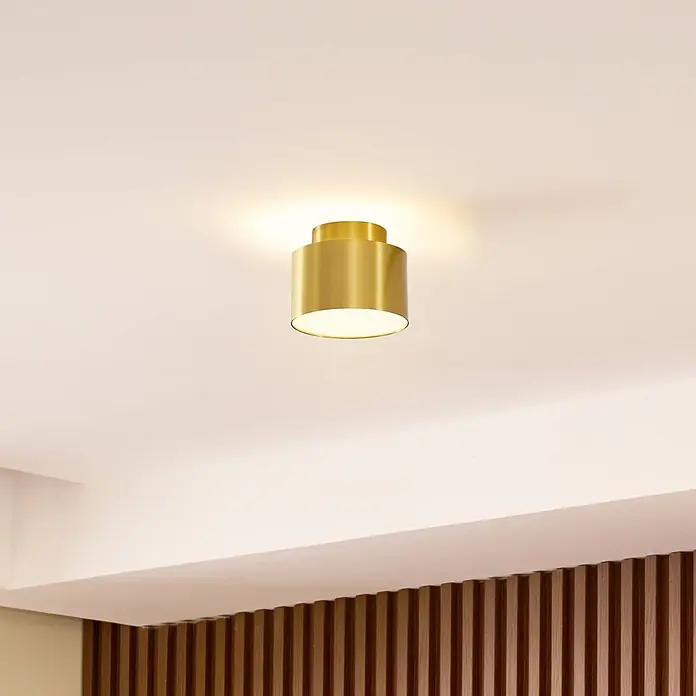 Lindby LED Aufbauleuchte gold Ø 11 cm, Aufbaustrahler, Deckenspot 15W LED -  - Eine zylindrische Deckenleuchte aus Messing ist an einer hellen Decke montiert und strahlt ein warmes Licht nach unten und oben ab.