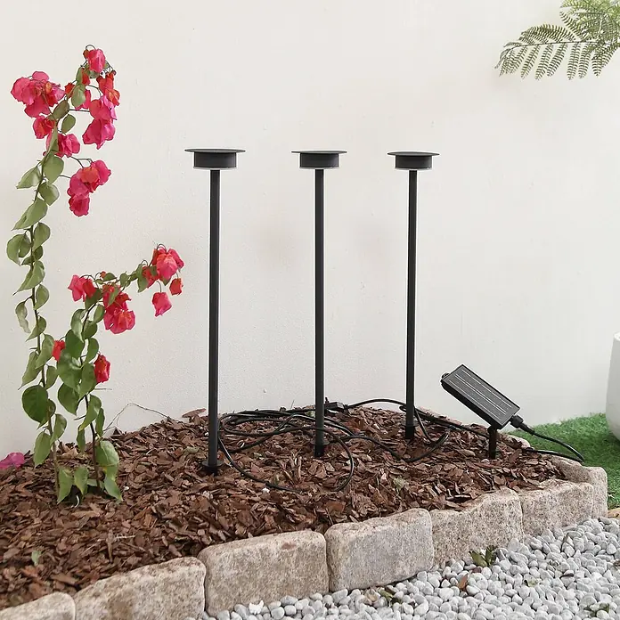 Lindby LED Solar Gartenlampe Erdspieß in schwarz matt, Erdspießlampe -  - Drei schwarze Solar-Gartenleuchten mit separatem Solarpanel, in einem Mulchbeet installiert.