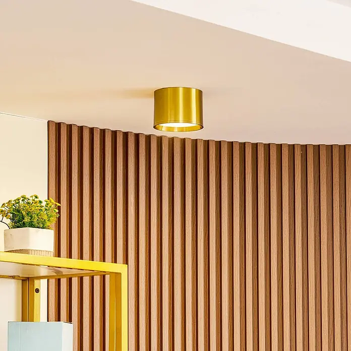 Lindby LED Aufbauleuchte gold Ø 12 cm, Aufbaustrahler, Deckenspot 15W LED -  - Goldene zylindrische Deckenleuchte an einer Decke über einer Holzlamellenwand.