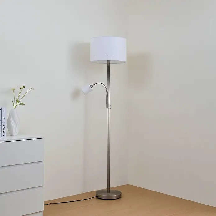 Lindby Stehlampe Leselampe in weiß, grau, up down Stehleuchte -  - Silberne Stehlampe mit weißem Uplight und verstellbarer Leselampe steht in einer Zimmerecke neben einer weißen Kommode.